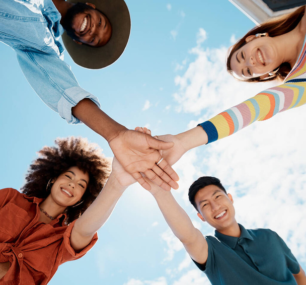 Low angle view of diverse group of people standing huddled together with hands piled in the middle. African American woman with an afro. Millennial social clique stacking hands in unity and support. - Photo, image