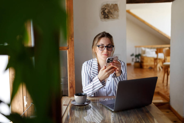 Szczęśliwa młoda bizneswoman siedząca przy stole z laptopem, trzymająca telefon komórkowy z klientem w biurze. Sprzedawczyni wykwalifikowanych menedżerów dzwoniąca do klienta, udzielająca profesjonalnej konsultacji. - Zdjęcie, obraz
