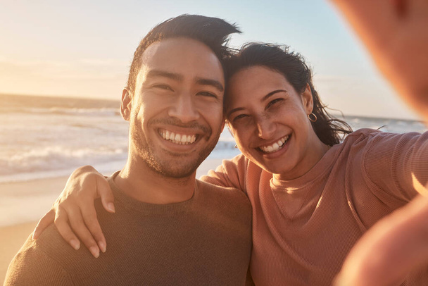 Portrait of a young diverse biracial couple taking a selfie at the beach and having fun outside. - Fotó, kép