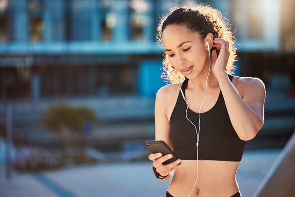 Τραβηγμένο πλάνο μιας ελκυστικής νεαρής αθλήτριας που ακούει μουσική ενώ είναι έξω για τρέξιμο στην πόλη. - Φωτογραφία, εικόνα