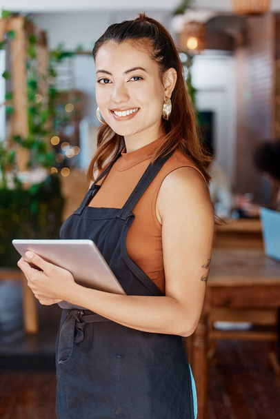 Young hispanic business owner using a wireless tablet in her retail store. Portrait of smiling entrepreneur standing in her restaurant using an online digital device. Young new business owner. - Foto, immagini