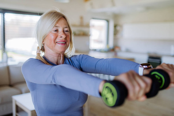 Una mujer mayor en forma haciendo ejercicio con pesas en casa, concepto de estilo de vida activo. - Foto, imagen