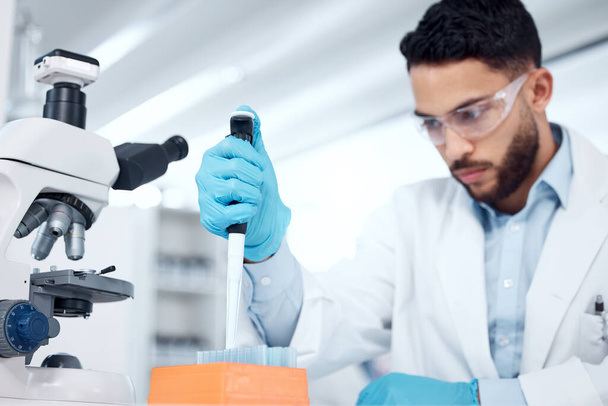 Een gemengde ras mannelijke wetenschappers dragen veiligheidsbril en een labjas tijdens het uitvoeren van medisch onderzoek experimenten met pipet en reageerbuizen in een lab. Registratie van zijn bevindingen voor toekomstig onderzoek. - Foto, afbeelding