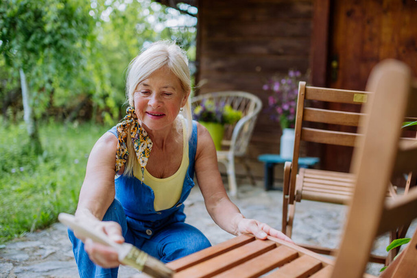 Une femme âgée nettoie les meubles de jardin et prépare le jardin pour l'été - Photo, image