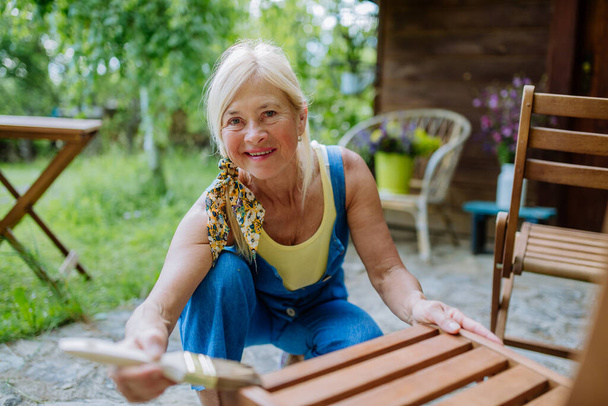 A senior woman cleaning garden furniture and getting the garden ready for summer - 写真・画像