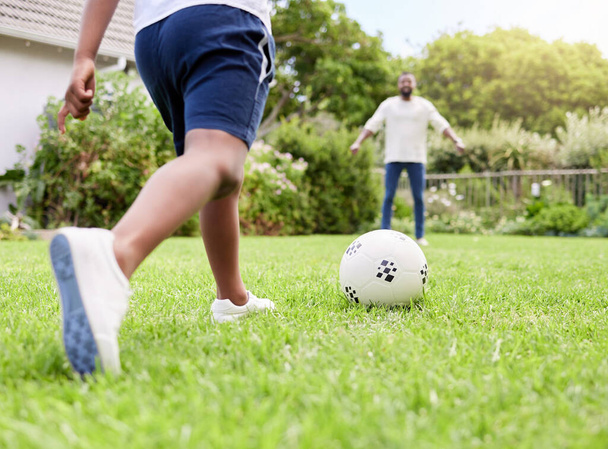 Κοντινό πλάνο ενός μικρού αγοριού να κλωτσάει μια μπάλα ποδοσφαίρου στον πατέρα του ενώ παίζαμε μαζί έξω.. - Φωτογραφία, εικόνα