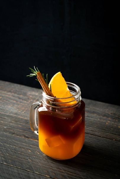 A glass of iced americano black coffee and layer of orange and lemon juice decorated with rosemary and cinnamon - Foto, afbeelding