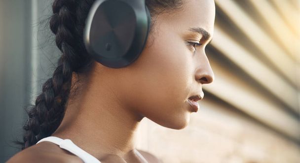 Primer plano de una joven hispana en forma escuchando música con auriculares mientras hace ejercicio en un entorno urbano al aire libre. Cara de atleta femenina enfocada y motivada lista para entrenar o correr - Foto, imagen