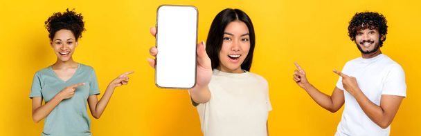 Panoramic photo of three multiracial people on isolated orange background.Asian girl shows smartphone with empty white mockup screen, indian guy and african american girl pointing their fingers at her - Foto, Bild