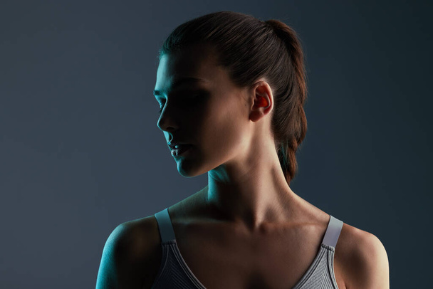 Schnappschuss einer attraktiven jungen Sportlerin, die im Studio vor grauem Hintergrund posiert. - Foto, Bild