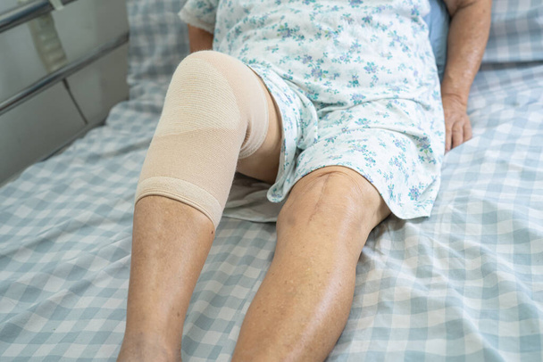 Asiatische Seniorin oder ältere Dame mit Knieschmerz im Bett auf der Krankenstation, gesundes starkes medizinisches Konzept. - Foto, Bild