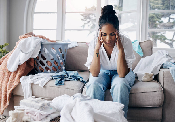 Shot of an attractive young woman sitting alone in her living room and feeling stressed wile doing the laundry. - Photo, image