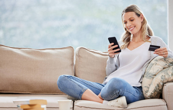 Shot of a young woman using a cellphone and credit card at home. - Foto, Bild