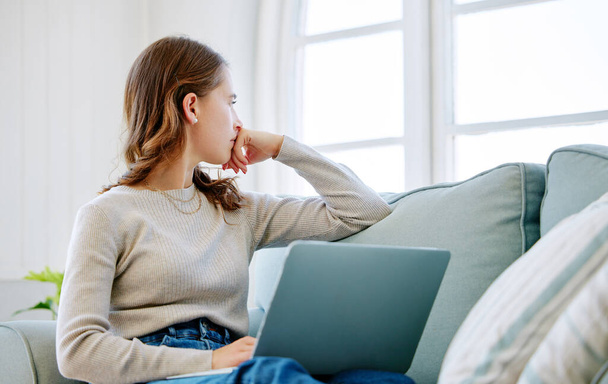 Обрезанный снимок привлекательной молодой женщины, смотрящей вдумчиво, расслабляясь дома на диване. - Фото, изображение