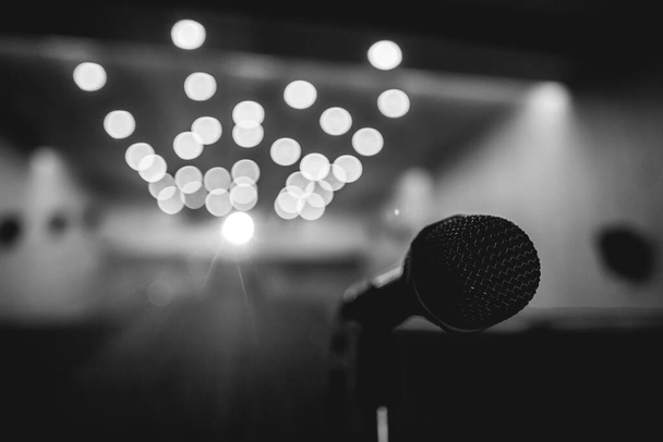 Closeup of microphone on stage of a big entertainment room with spotlight and blurry lights (in black and white) - Фото, изображение