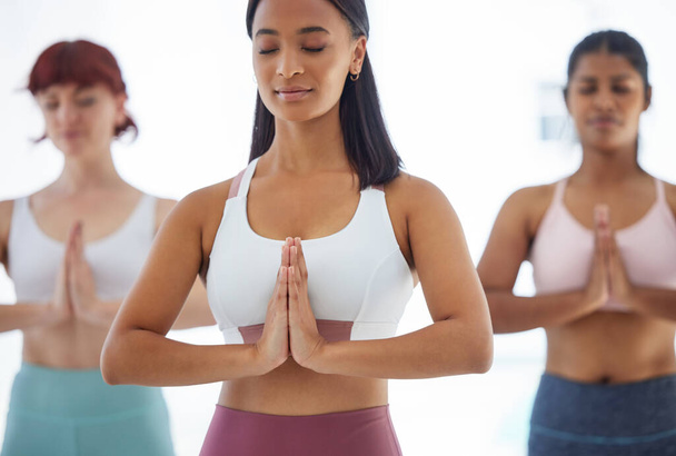Снимок группы спортивных молодых женщин, медитирующих во время тренировки в студии йоги. - Фото, изображение