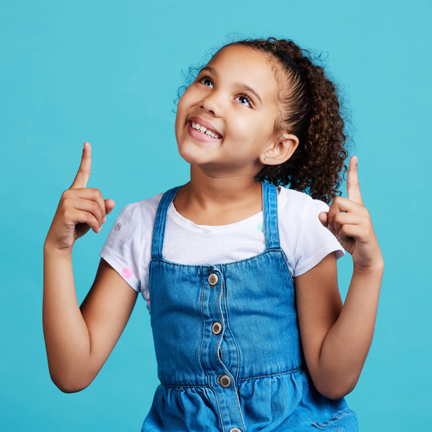 Shot of an adorable little girl pointing at something while standing against a blue background. - Foto, Imagen