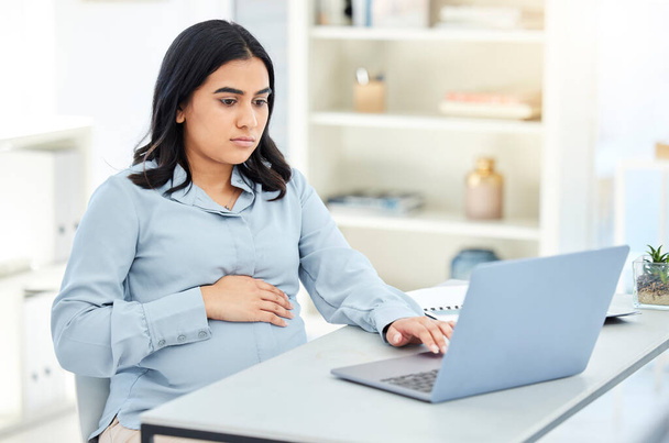 Foto van een zwangere zakenvrouw aan het werk op een laptop in een kantoor. - Foto, afbeelding