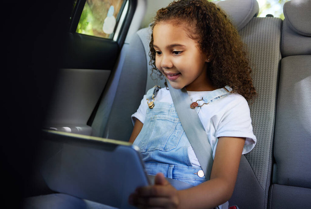 Cropped shot of an adorable little girl using her tablet while sitting in the backseat of a car. - Photo, image