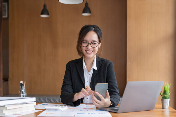 Asian woman holding smart phone while using calculator for business financial accounting calculate money bank loan rent payments manage expenses finances taxes doing paperwork concept, close up - Photo, Image