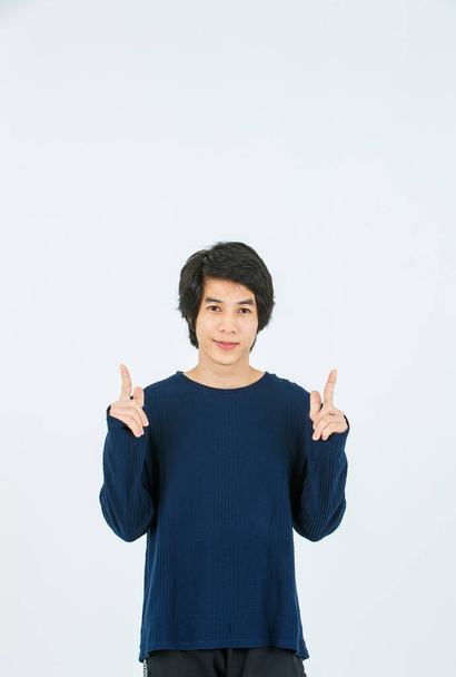 Estudio de tiro de Asiático joven guapo delgado adolescente moda modelo masculino en camisa de manga larga de pie sonriente cogido de la mano señalando los dedos en el espacio de copia en blanco presentando el producto sobre fondo blanco. - Foto, imagen