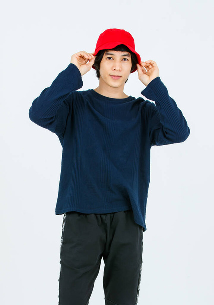Full body studio shot Asian young handsome slim teenager fashion male model in street style outfit long sleeve shirt standing posing smiling holding hand adjusting red bucket hat on white background. - Photo, Image