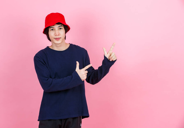 Portrait studio shot Asian young urban teen fashion male model in street style outfit long sleeve shirt red bucket hat standing crossed arms smiling look at camera on pink background - Foto, Bild