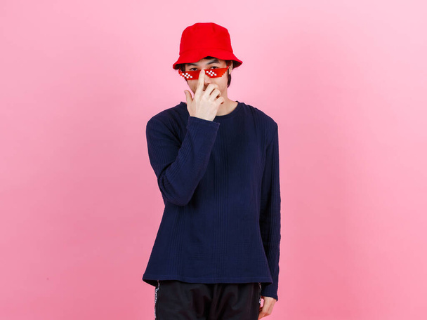 Portré stúdió lövés ázsiai fiatal városi tini divat férfi modell utcai stílus ruha hosszú ujjú ing piros vödör kalap vicces szemüveg álló keresztbe karok mosolygós nézni kamera rózsaszín háttér. - Fotó, kép