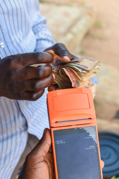 Foto van Afrikaanse handen tellen van contant geld, geld, of Nigeriaanse valuta, terwijl een andere hand is het houden van een digitaal verkooppunt machine die bekend staat als POS-apparaat - Foto, afbeelding
