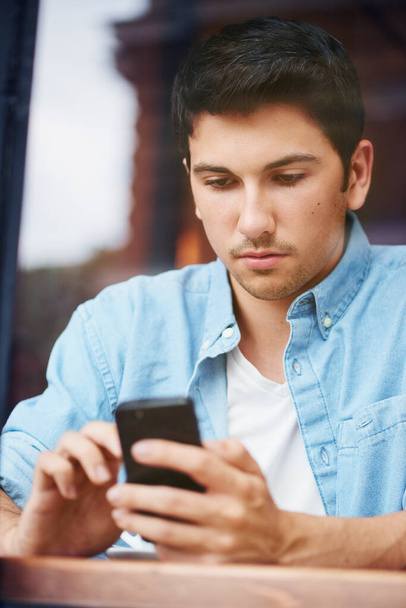 One mixed race handsome young man using his mobile phone while sitting outside in the city. Hispanic male texting and browsing social media while using the internet to order food online for delivery. - Fotoğraf, Görsel