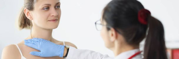 Retrato de una mujer rubia en la cita con un médico siendo examinada por un profesional médico. La enfermera toca el cuello y el pecho. Proporcionar ayuda, concepto de salud - Foto, Imagen