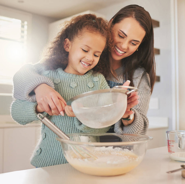 Shot van een moeder bakken met haar dochter in hun keuken thuis. - Foto, afbeelding