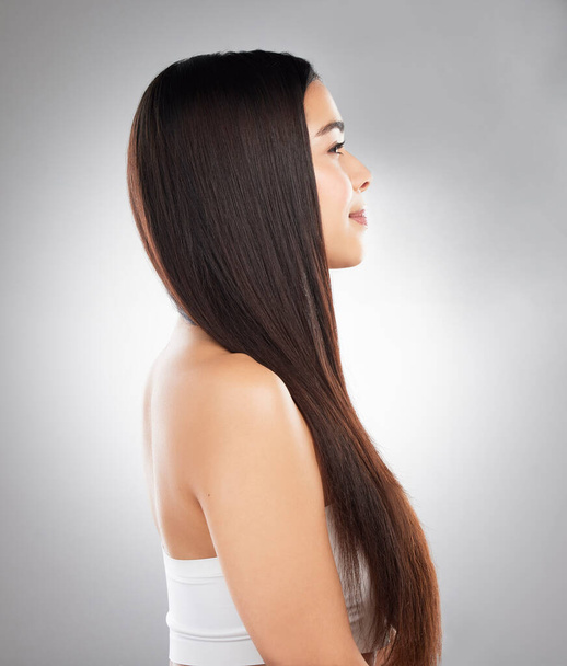 Studio shot of a beautiful young woman showing off her long silky hair against a grey background. - 写真・画像