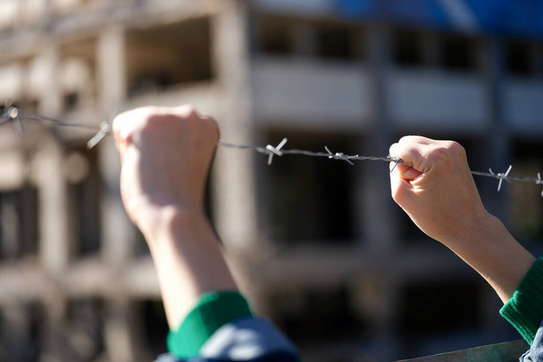 Close-up of female hands holding security barbedwire fence, wire with clusters of short, sharp spikes. Fence or warfare obstruction, correctional institution concept - Photo, image