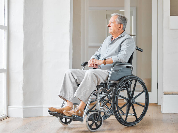 Shot of a senior man sitting in a wheelchair and looking thoughtfully out the window at home. - Foto, immagini