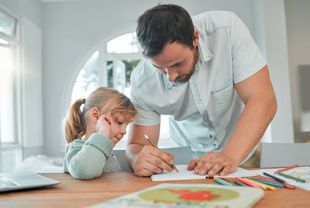 Καυκάσιος άντρας γράφει σε βιβλίο ενώ βοηθάει την κόρη του με εργασίες και εργασίες. Κοριτσάκι που μαθαίνει και σπουδάζει στο σχολείο με τον μπαμπά. Γονέας που διδάσκει παιδί στο σπίτι. - Φωτογραφία, εικόνα
