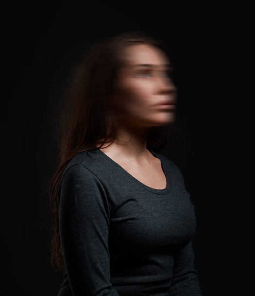 Studio shot van een vrouw staande tegen een zwarte achtergrond met een wazig gezicht. - Foto, afbeelding