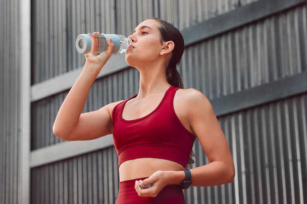 Cropped shot of an attractive young female athlete drinking water while running outdoors. - Foto, imagen