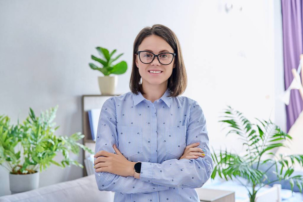 Portrait of confident young woman looking at camera at home. Smiling successful cheerful business female with crossed arms. Work, business, career, intelligence, people concept - Фото, зображення