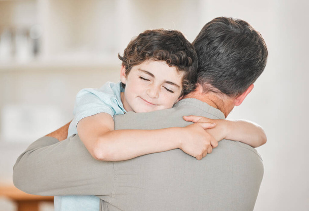 Τραβηγμένο πλάνο ενός αξιολάτρευτου αγοριού που αγκαλιάζει τον πατέρα του με αγάπη στο σπίτι. - Φωτογραφία, εικόνα