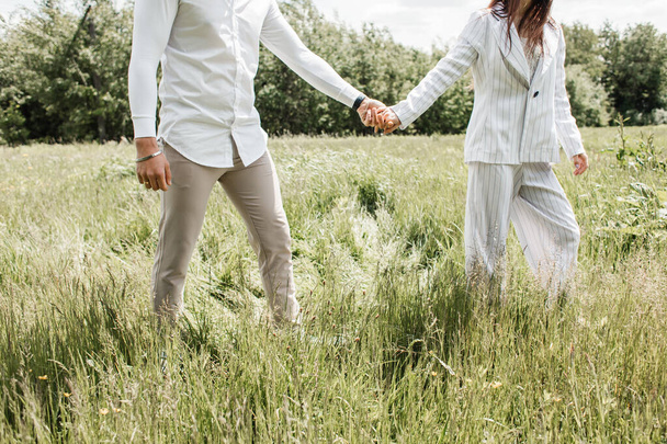 Een stel dat elkaars hand vasthoudt loopt door een veld met groen gras. Foto in lichte kleuren - Foto, afbeelding