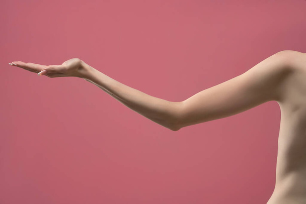 Young woman's stretched skinny arm and open palm holding imaginary product. Isolated on pink background. - Foto, Imagen