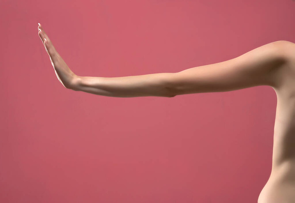 Der ausgestreckte dünne Arm der jungen Frau mit Stop-Geste. Vereinzelt auf rosa Hintergrund. - Foto, Bild