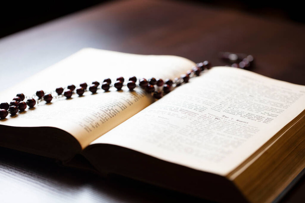 Cristianismo tema oración. Mujer cristiana con la Biblia rezando con las manos cruzadas manteniendo rosario. - Foto, Imagen