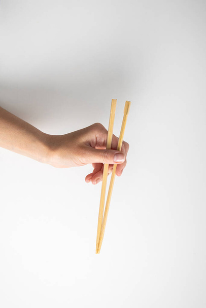 Woman's hand holding two chinese chopsticks on a white background. - 写真・画像