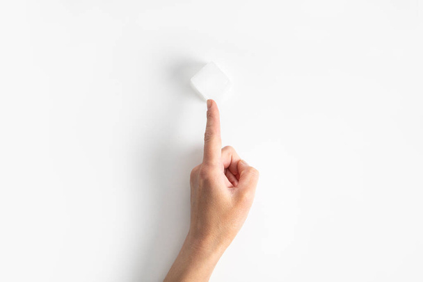 Woman's hand points a finger at an ice cube on a white background. Top view, flat lay. - Foto, Imagem