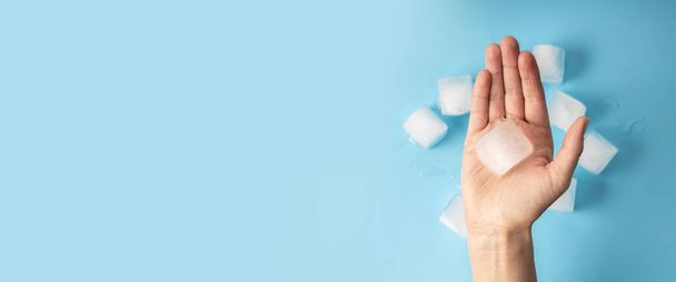 Woman's hand holding an ice cube on a blue background. Top view, flat lay. Banner. - Foto, Bild