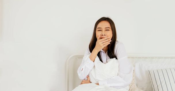 Kadınlar her gün geç uyur: Asyalı genç kadın oturur ve ellerini uzatarak ağzını kapatır, çünkü çok geç uyur ve sabahları yorgun düşer.. - Fotoğraf, Görsel