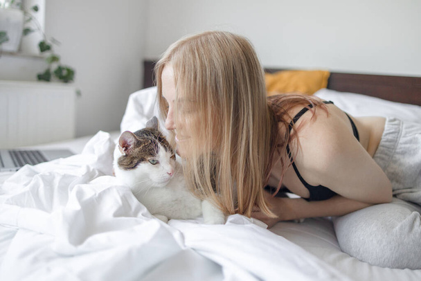 Vrouwelijke knuffelende vermoeide droevige kat in handen op het bed thuis. Blijf thuis. Blijf veilig. Liefde, zorg, adoptie - Foto, afbeelding