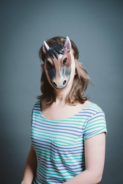 Fiatal nő maszkot visel szürke háttérrel a stúdióban. - Fotó, kép
